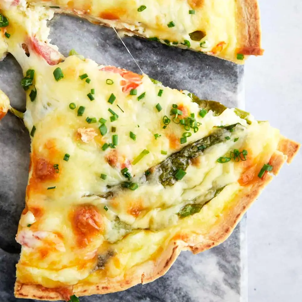 A slice of tortilla quiche bake with layers of eggs, cheese, and vegetables, served on a plate.