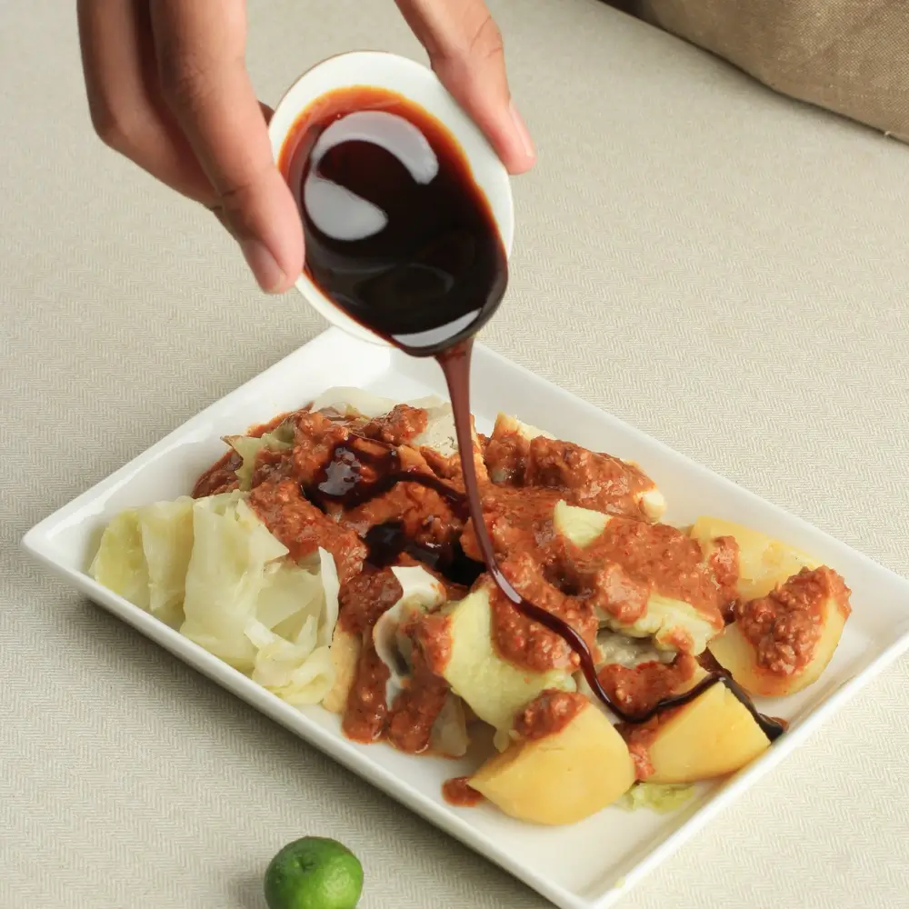 A bottle of homemade soy sauce, rich in color and texture, next to a small dish for serving.